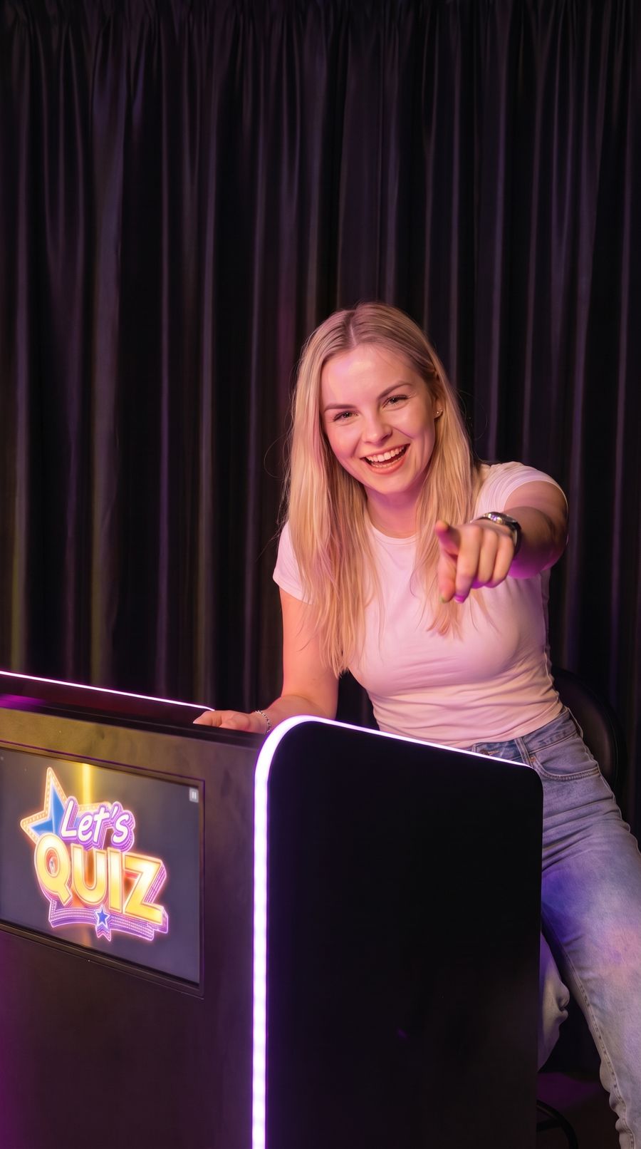Uśmiechnięta graczka przy stanowisku Let's Quiz wskazuje na widza